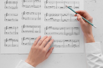 Female hands with pencil and music sheets on light background