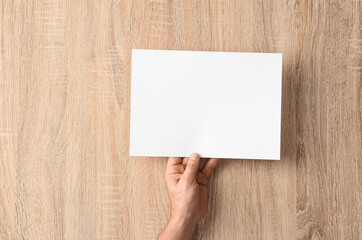 Obraz premium Male hand with blank paper sheet on wooden background