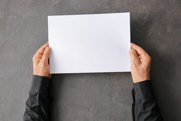 Male hands with blank paper sheet on dark background