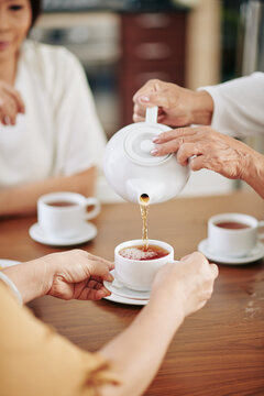 Close-up image of senior woman pouring hot black tea in cups for her female friends