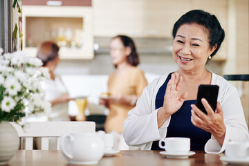 Portrait of happy senior Vietnamese woman waving with hand when video calling her friends or family members