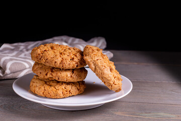 A stack of oatmeal cookies in a saucer on a wooden table on a dark background.