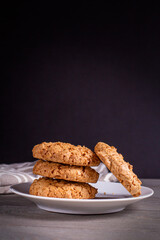 A stack of oatmeal cookies in a saucer on a wooden table on a dark background.