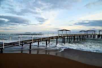 View from beach to water of sea, waves with white foam, pierce and sky with clouds in a nice evening.