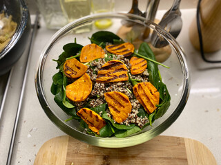 Homemade Grilled Sweet Potato Salad with Baby Spinach and Three Color Quinoa Seeds in Glass Bowl on Kitchen Surface.
