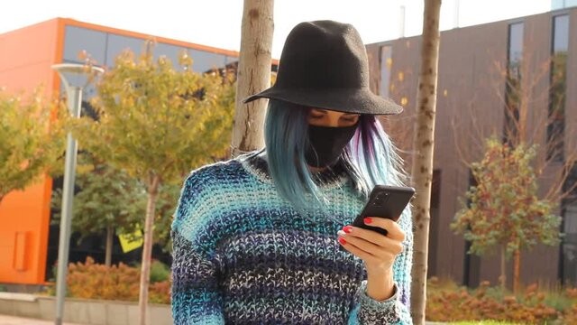 girl with blue hair in Protective black Mask and hat with smartphone. Urban fashion outfit.