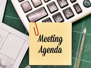 Text Meeting Agenda written on yellow paper note with a pen and calculator.Business concept.