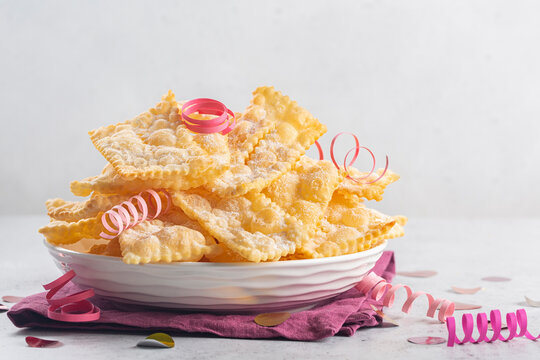 Angel wings or frappole or chiachiere. Traditional sweet crisp pastry deep-fried and sprinkled with powdered sugar. Carnival food tradition. Decorated with pink paper serpentine.