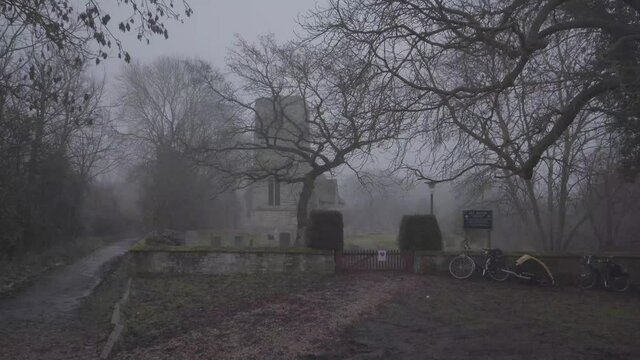 Stone church with cementery in england during a foggy day. Dark forest in winter