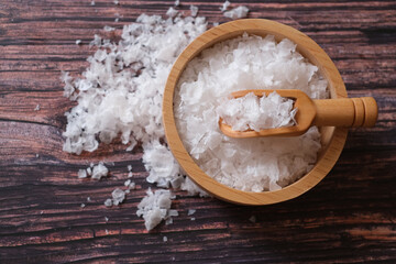 Flower of salt, is a salt that forms as a thin, delicate crust on the surface of seawater in the wooden scoop and wooden bowl on wooden background. Selective focus. 