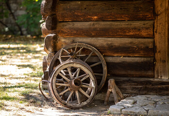 Obraz premium Wooden wheels from an ancient cart standing in front of the wall of a wooden country cottage