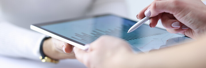 Female hand holds stylus over included tablet with business records together with colleague....