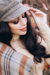 Beautiful and stylish girl model with makeup in a beige dress and a scarf in the form of plaid in the park