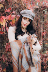 Beautiful and stylish girl model with makeup in a beige dress and a scarf in the form of plaid in the park