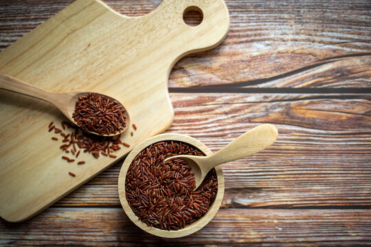 Red rice and wooden spoon in wooden bowl and red rice in wooden spoon on cutting board.