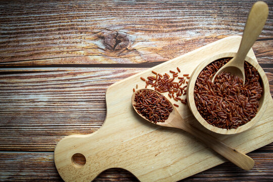 Red rice in wooden spoon and wooden bowl on Cutting board.