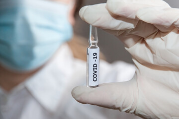 An ampoule with the Covid-19 vaccine on the background of a man in a white coat and mask