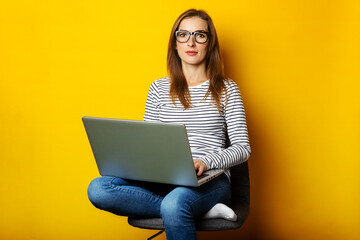 Young woman sitting on chair and holding laptop on isolated yellow background