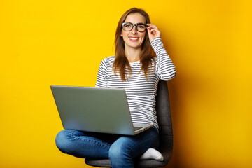 Young woman on chair working at laptop on yellow background