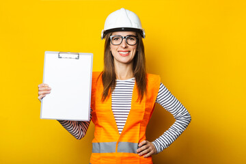 Young woman in a vest and hard hat holds a clipboard on a yellow background. Construction concept, new building. Banner