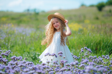 little girl in a straw hat in a purple field in summer