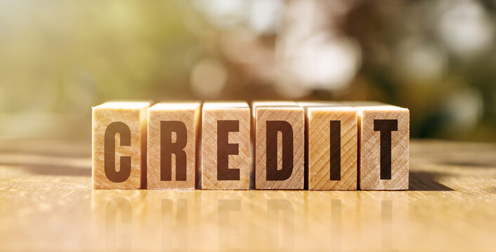 Word CREDIT made with building wooden blocks on table in sunlight.