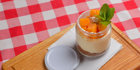 Healthy layered dessert with cream cheese and persimmon served in a small glass jar on table with red plaid tablecloth.
