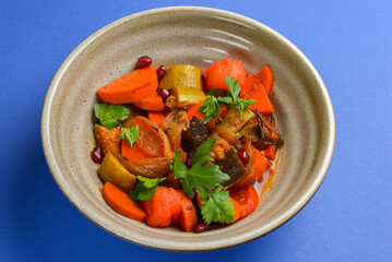 Baked vegetable salad in a cermaic bowl over blue background. Delicious healthy autumn or winter salad.