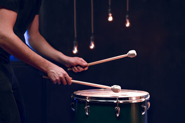 The drummer plays with mallets on floor tom in dark room.