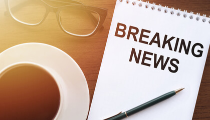 BREAKING NEWS - text on paper with cup of coffee and glasses on wooden background in sinlight.