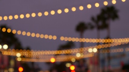 Defocused illuminated electric garland, palm trees silhouettes, Oceanside California USA. Ocean beach tropical pink sunset, pacific coast purple twilight sky. Los Angeles vibes. Bulb lights glowing.