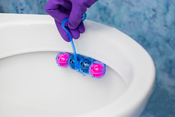 Person in purple protective rubber gloves holds multi-colored balls of toilet bowl cleaner....