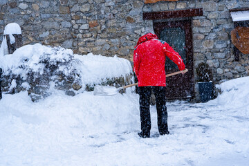 Man with snow shovel cleans sidewalks in winter near house. Winter time, snowfall. France Europe.