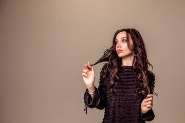 Obraz premium beautiful slender young girl with black long hair on a one-ton beige background. woman in brown trousers and black blouse with open back.