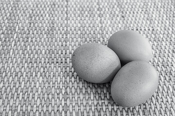 Three eggs placed on a wicker surface with empty space on the left. Black and white.