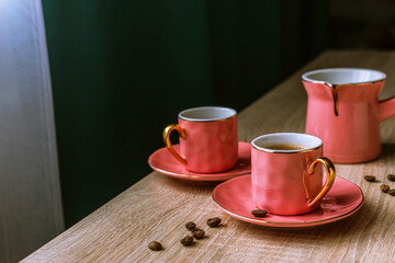 Pink ceramic coffee set - turk and two cups with espresso on wooden table. Tableware in the English style