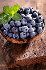 Bowl of fresh blueberries on rustic wooden board. Organic food blueberries and mint leaf for healthy lifestyle.