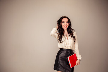 a beautiful young girl with red lips holds a red notebook in her hands. student. businesswoman on isolated gray background