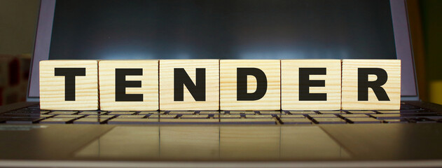 Word TENDER. Wooden cubes with letters isolated on a laptop keyboard. Business Concept.