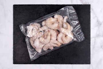 Products in vacuum packaging on black slate board. Frozen shrimps, vacuum sealed food ready for sous vide cooking. Sous-vide, new technology cuisine in quarantine time