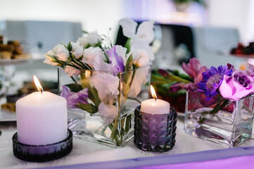 Obraz na płótnie Canvas Festive table decorated with composition of violet, purple, pink flowers and greenery, candles in the banquet hall. Table newlyweds in the banquet area on wedding party.
