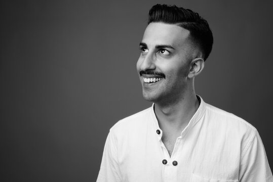 Young handsome Iranian man with mustache against gray background