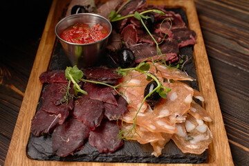 Cold cuts, sausage, basturma, smoked meat, with sauce and olives, on a wooden board, on a wooden background
