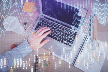 Double exposure of man's hands typing over computer keyboard and forex graph hologram drawing. Top view. Financial markets concept.