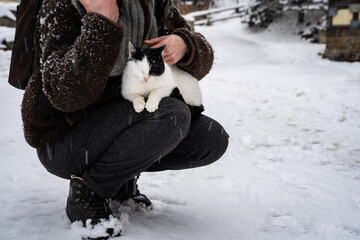 A black and white cat sitting on a woman's lap outside on a snowy day