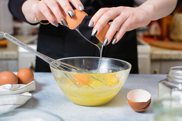 cook's hands break an egg over a glass bowl of dough