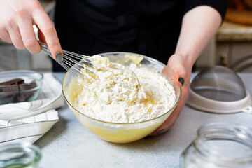 the chef holds a metal whisk and a glass bowl with flour dough in his hands