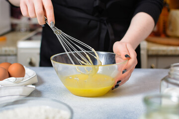 the cook whips the egg-oil mixture with a whisk to prepare the dough in a glass bowl