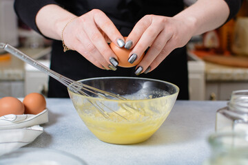 the cook's hands hold a whole egg over a glass bowl of dough