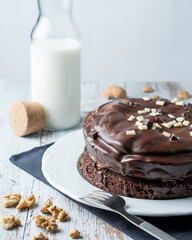 Chocolate and brownie cake witha open bottle of milk, nuts and a fork